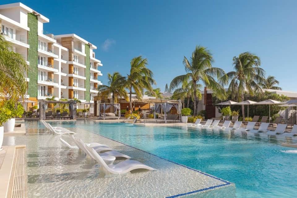 Modern resort pool with shallow entry, palm trees, white building with green accent wall