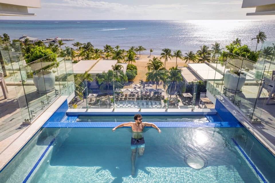 Man swimming in rooftop infinity pool with ocean and palm trees in background