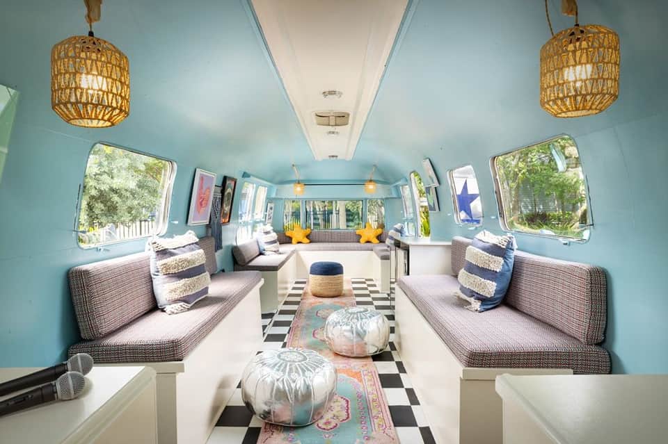 Turquoise vintage airstream trailer interior with dual seating, woven pendant lights, and windows