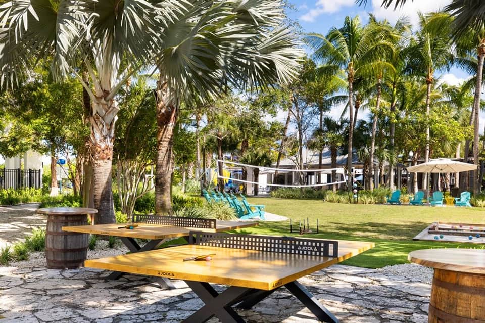 Lawn games area with cornhole boards under tall palm trees and wooden furniture