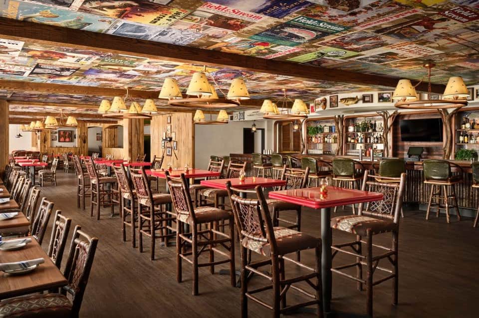 Rustic lodge dining room with red tables, wooden chairs, exposed beams, and vintage decor throughout.