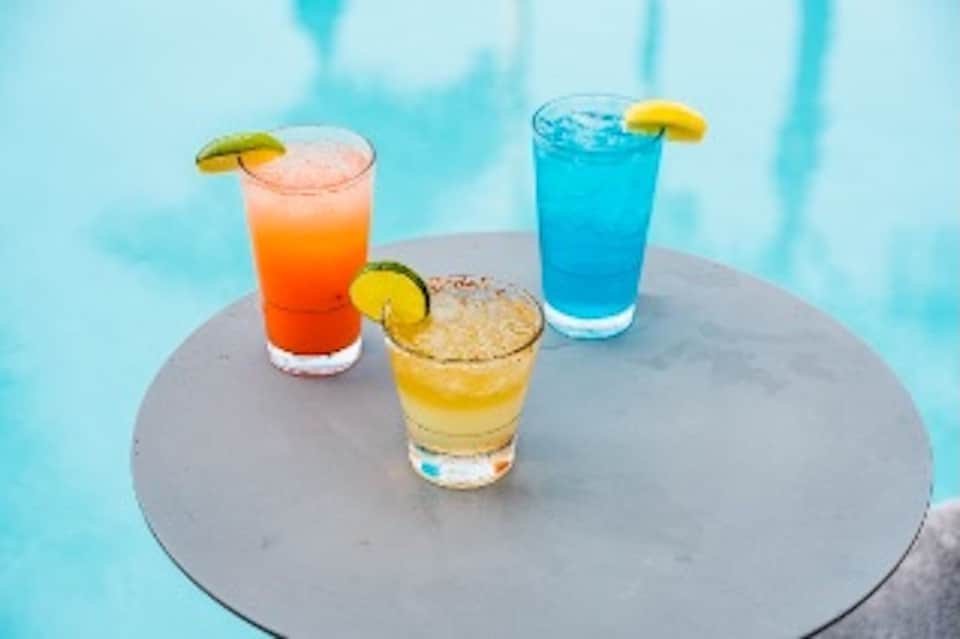 Three colorful cocktails with citrus garnishes on table poolside at sunset