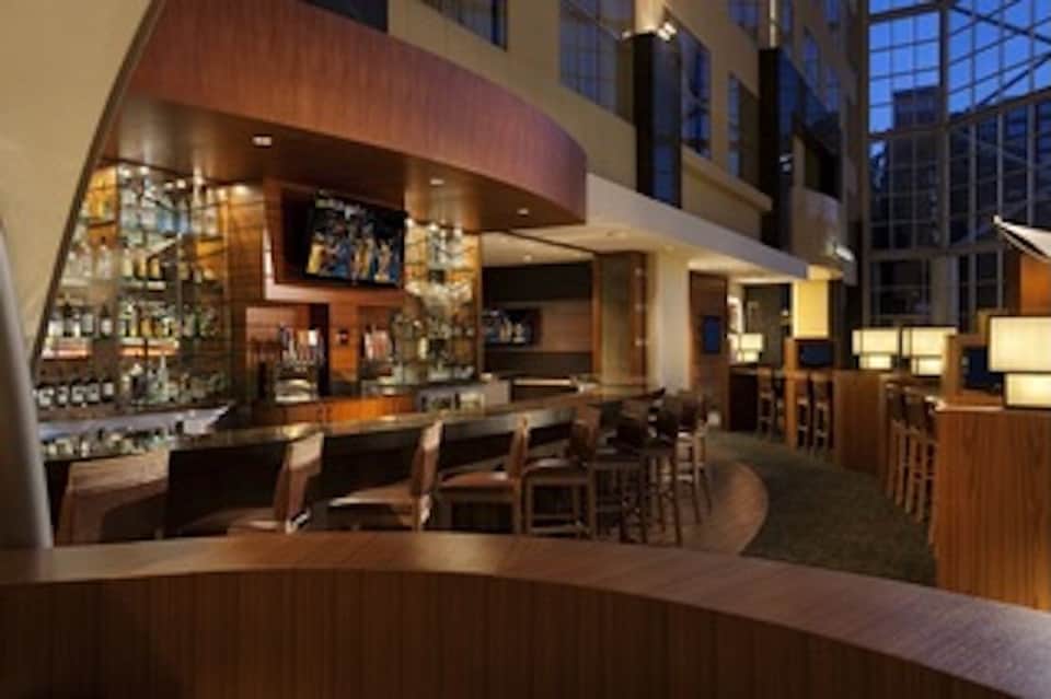 Modern hotel bar interior with wood finishes, ambient lighting, and bottle displays