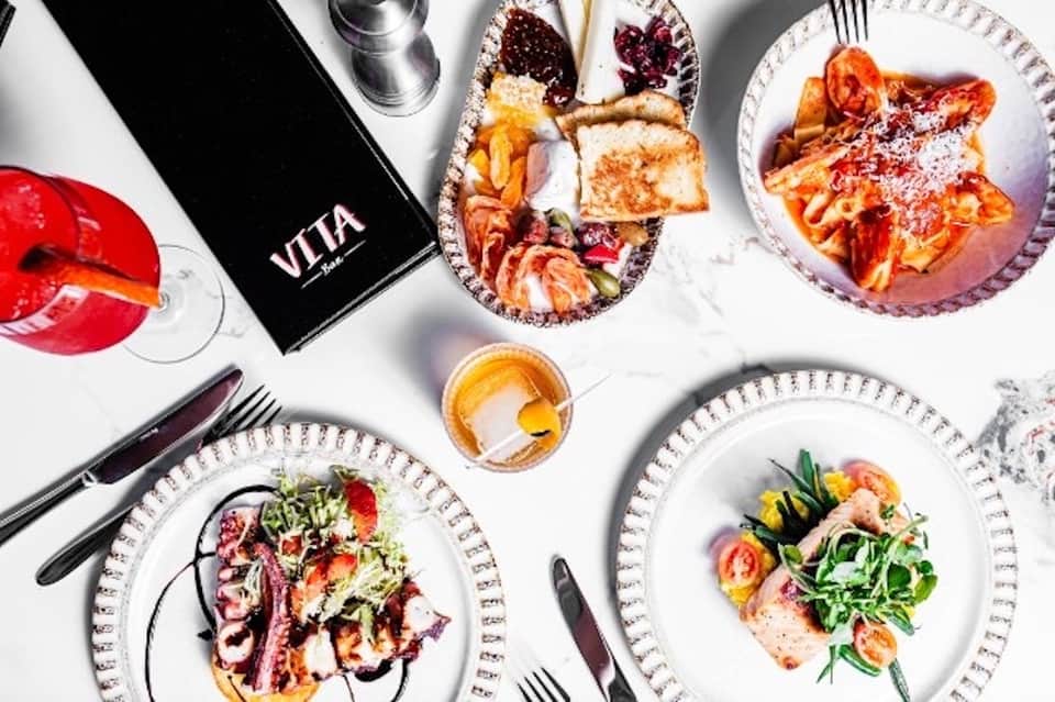 Overhead view of gourmet restaurant dishes, cocktails, and menu on white tablecloths