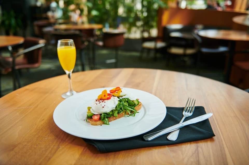 Plated brunch dish with avocado toast, egg, and citrus juice on wooden table in bright restaurant