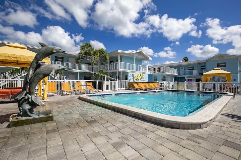 Pool area with yellow lounge chairs, dolphin statue, white railings, and blue sky at coastal resort.