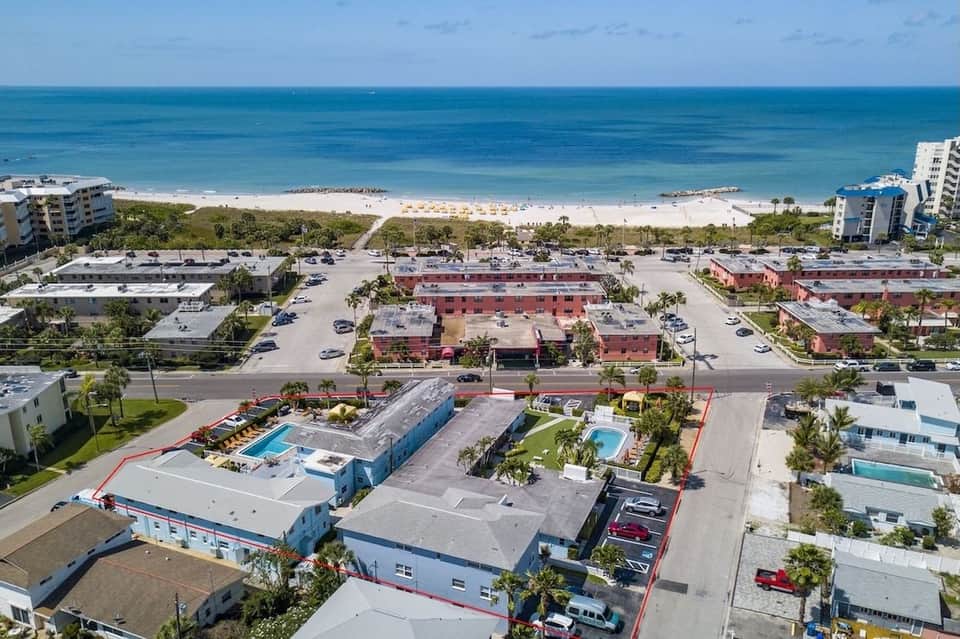 Aerial view of beachfront motel complex near sandy beach with red-roofed buildings and palm trees.