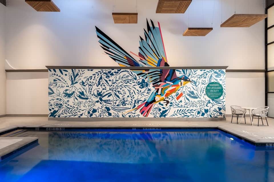 Indoor hotel pool with colorful bird mural and decorative wooden ceiling panels above