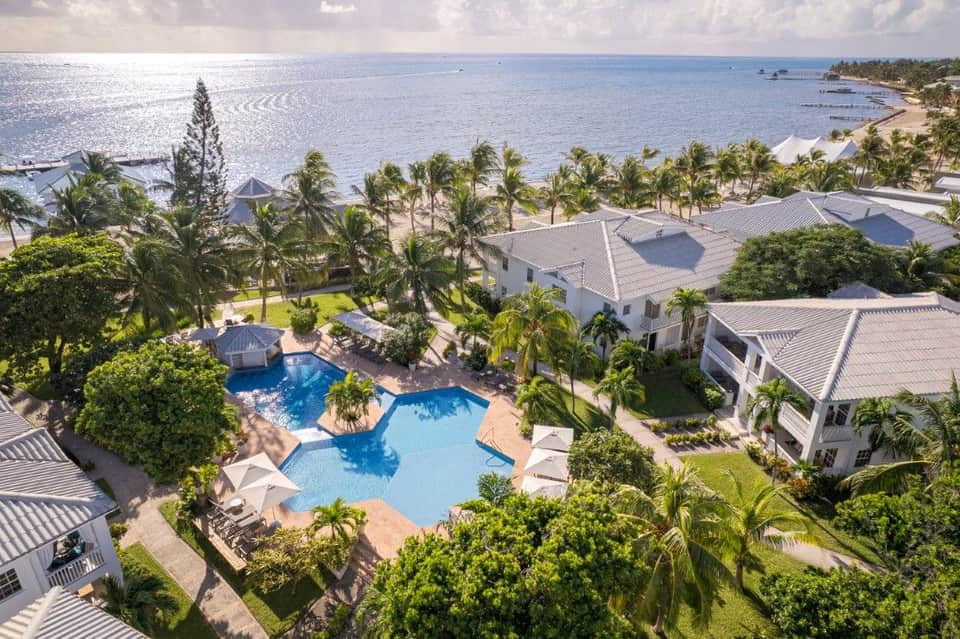 Aerial view of coastal resort with curved pool, white villas, beach access, and palm tree landscaping