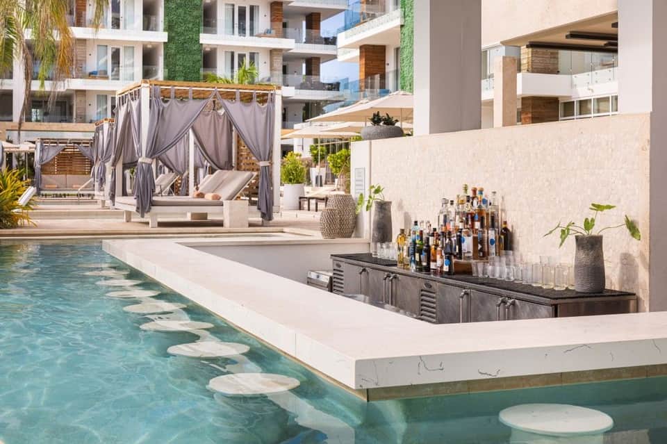 Luxury resort pool with swim-up bar, draped cabanas, and modern multi-story buildings with green vertical gardens