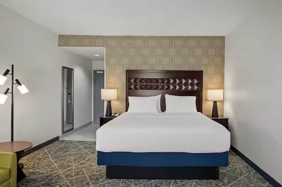 Hotel bedroom with queen bed, geometric headboard, patterned wallpaper, and modern furnishings
