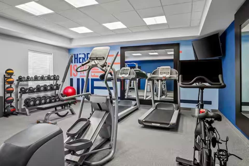Hotel fitness center with cardio equipment, dumbbells, exercise bike, and motivational wall signage