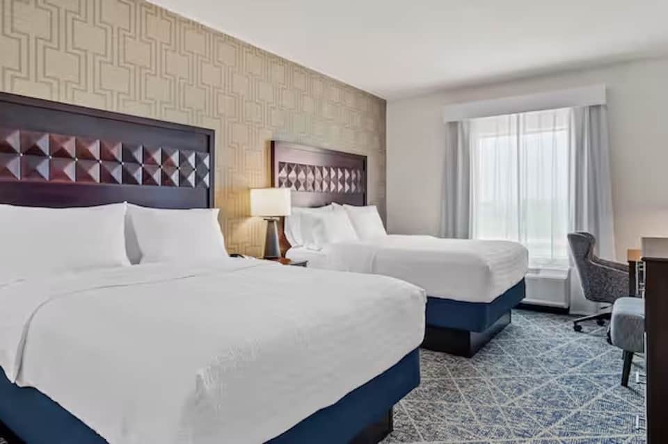 Hotel double queen room with white bedding, blue bed base, patterned wallpaper, and balcony access