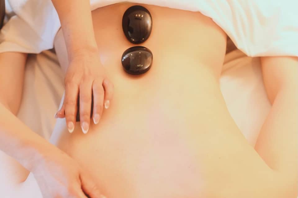 Therapist placing two heated black massage stones on client's back during spa treatment
