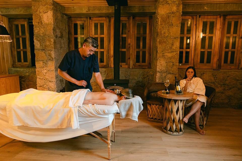 Male therapist performing massage on female client while spa attendant watches from nearby table
