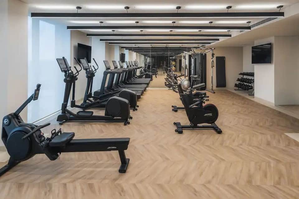 Modern gym with rows of exercise bikes, ellipticals, and strength training equipment on wood flooring