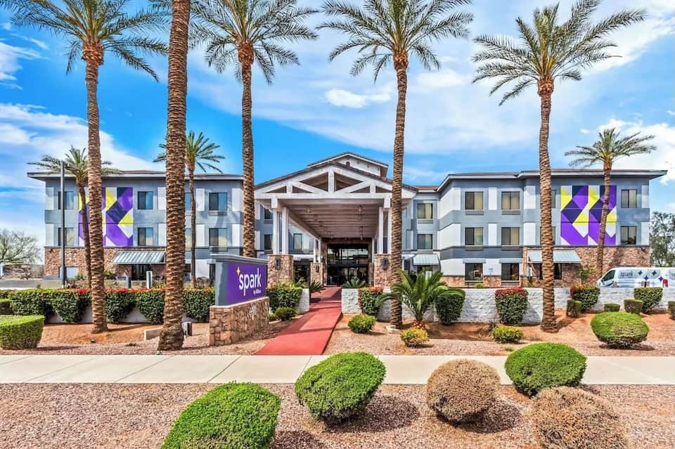 Contemporary hotel exterior with white and gray facade, purple geometric patterns, palm trees, and red entrance walkway