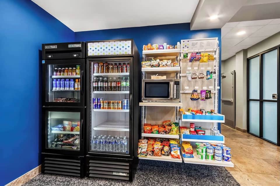 Hotel convenience store with refrigerated beverage cases, wall-mounted snack displays, and blue accent wall