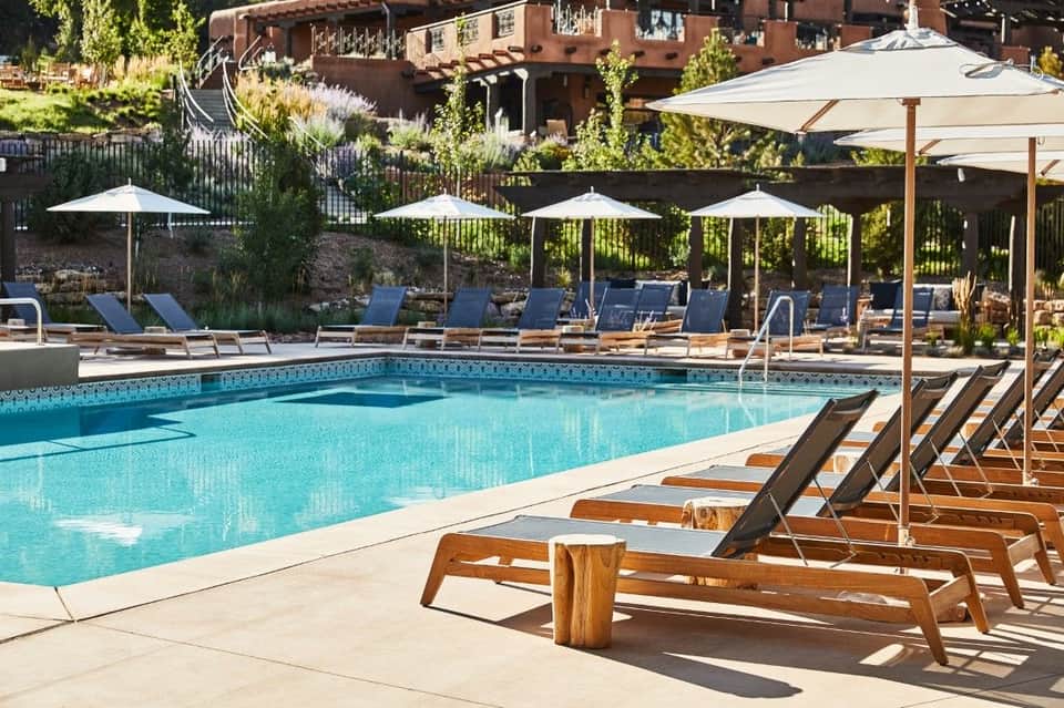 Lap pool with rows of wooden loungers, white umbrellas, and rocky hillside landscape