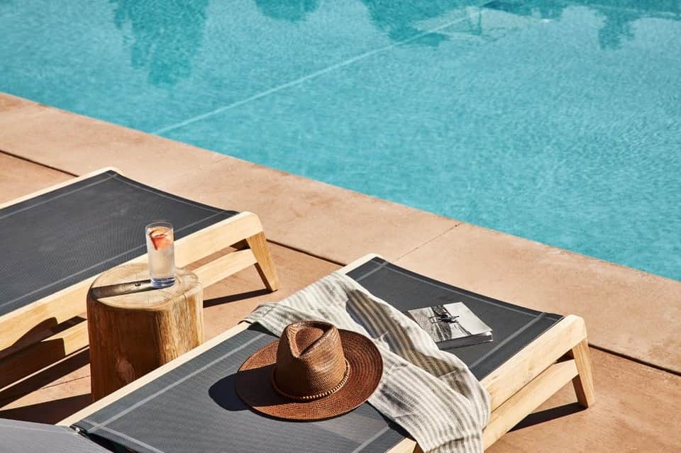 Wooden lounger poolside with hat and drink, turquoise pool water in background