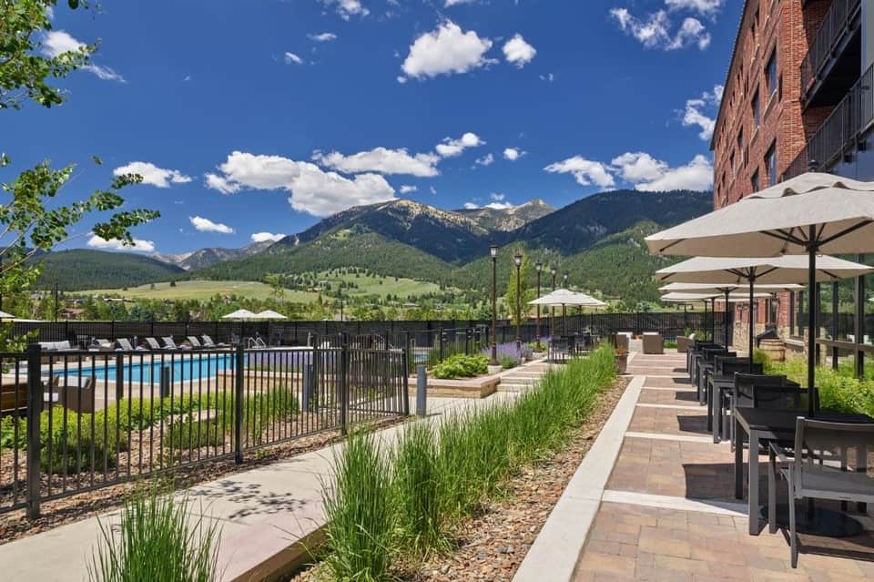 Patio dining area with mountain views, black fencing, umbrellas, and landscaping along pool