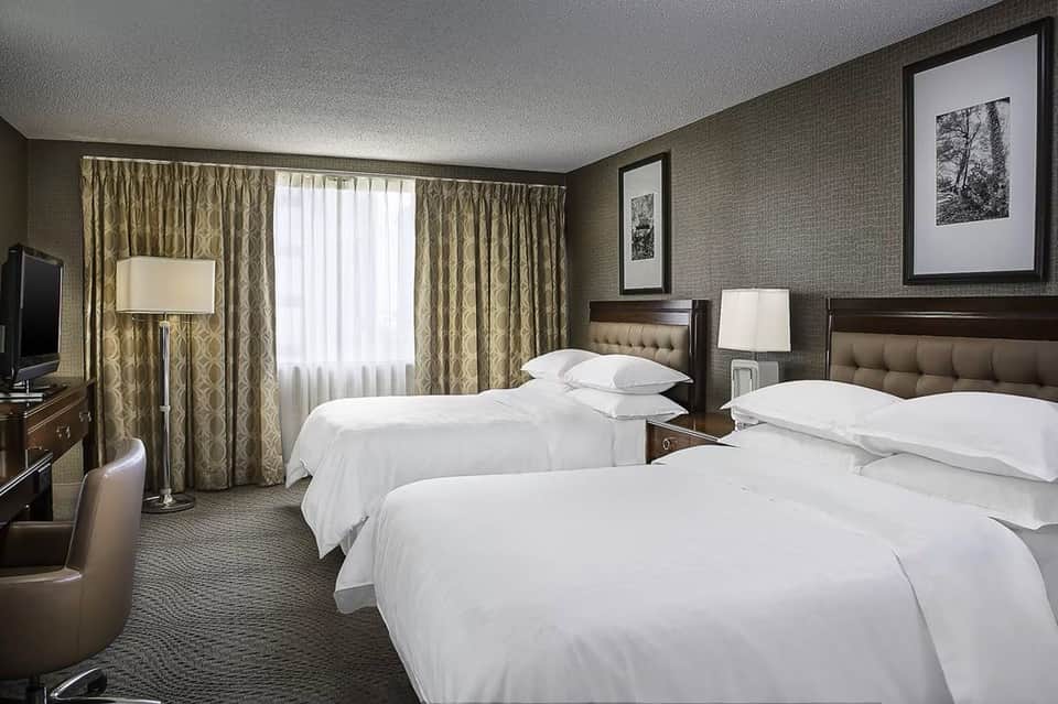 Hotel double room with two queen beds, patterned curtains, desk, and traditional furnishings in neutral tones