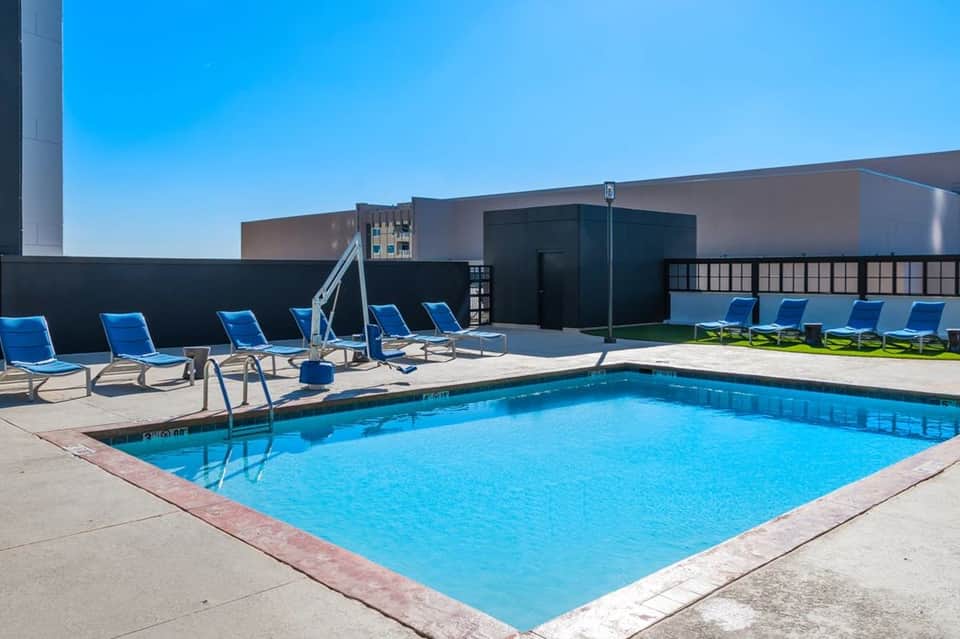 Rooftop pool with blue lounge chairs, umbrellas, and modern building structures under clear sky