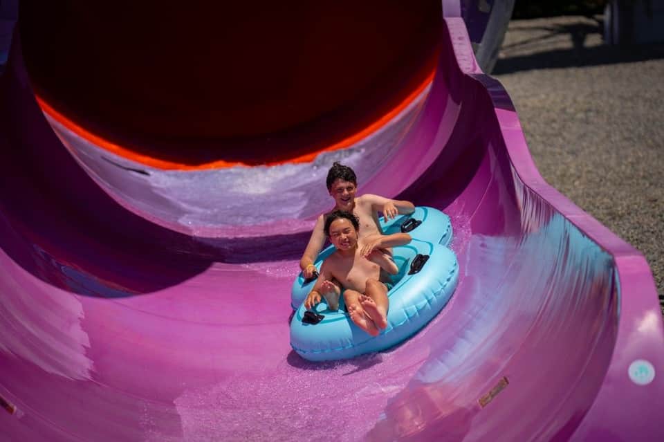 Two children on a blue inflatable tube sliding down a vibrant purple water slide