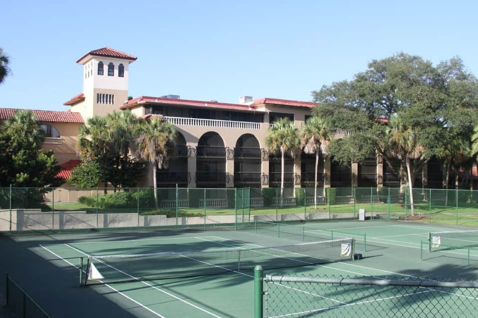 Spanish colonial-style building with arched windows and red tile roof overlooking tennis courts