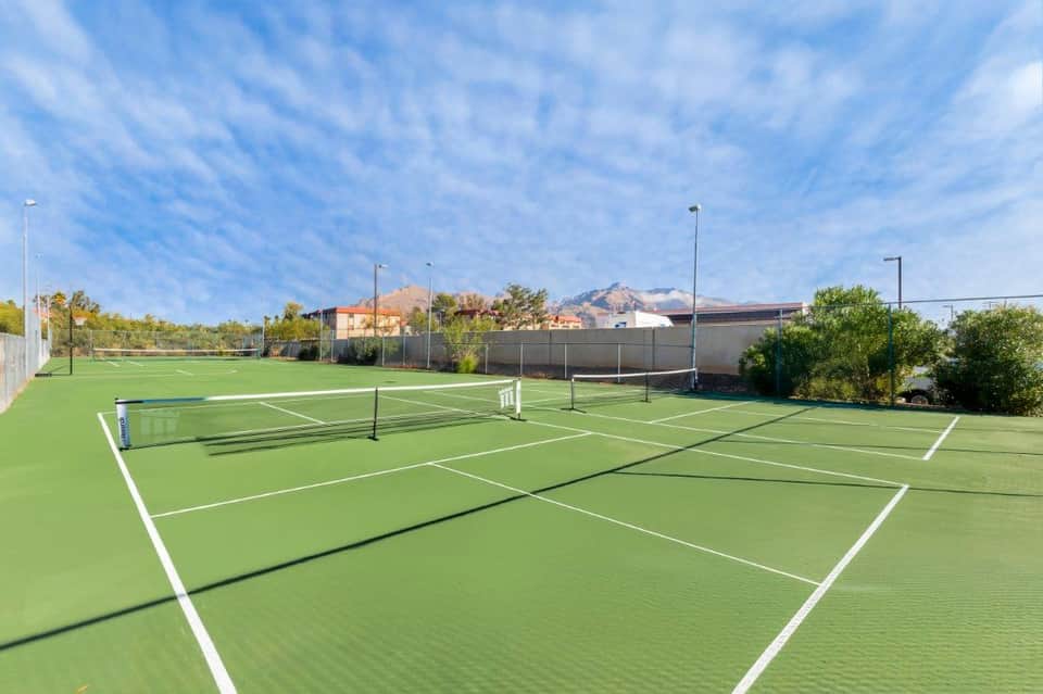 Multiple professional tennis courts with white line markings and net posts under blue sky