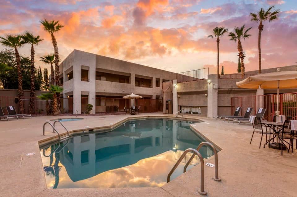 Resort pool at sunset with palm trees, lounge chairs, and modern concrete building