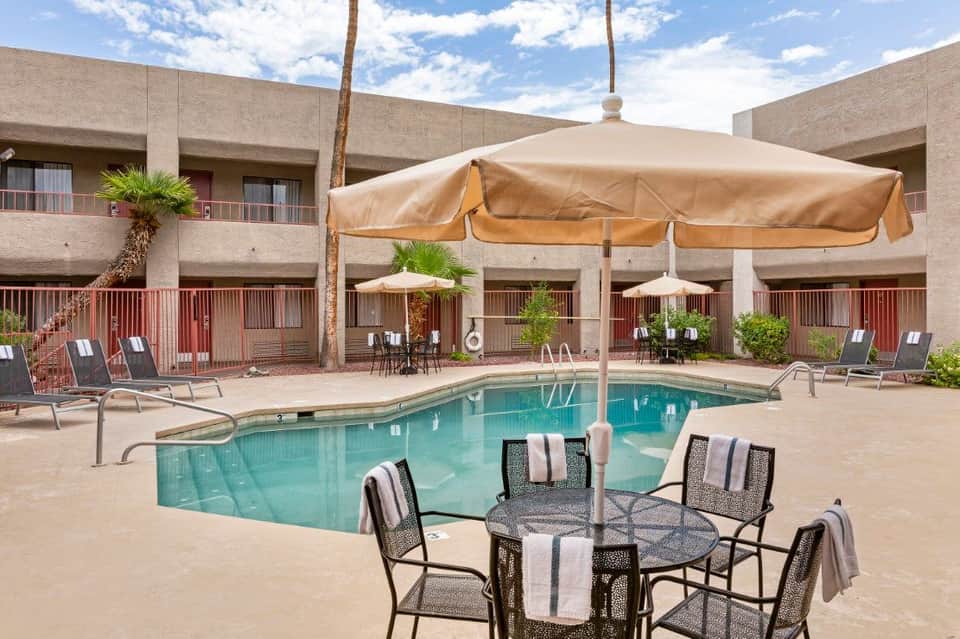 Outdoor pool with large umbrella, lounge chairs, and desert-style resort building