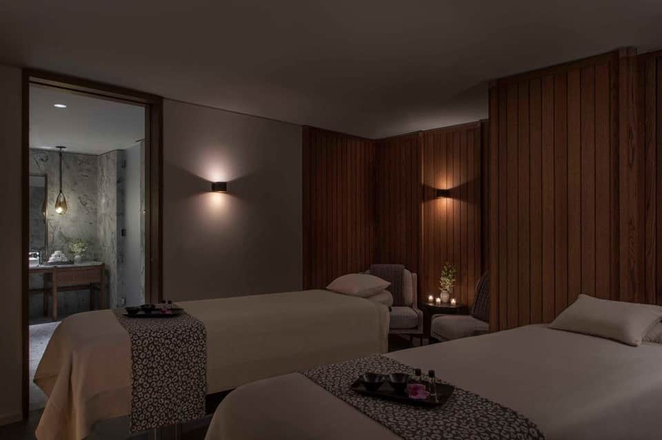 Luxury spa bedroom with dual beds, wood paneling, soft lighting, and ensuite bathroom