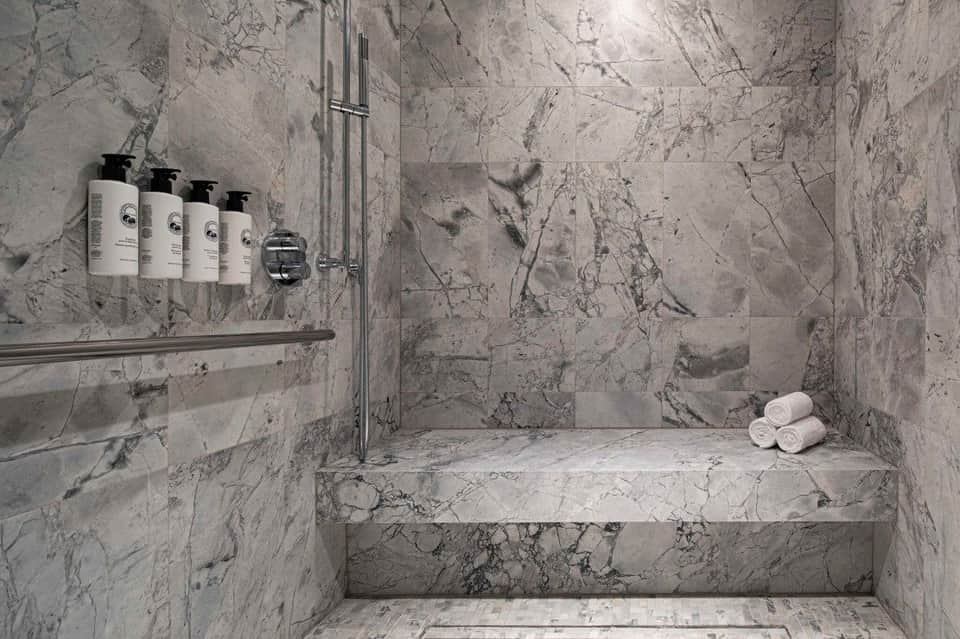 Marble spa shower with premium toiletries and rolled white towels on bench
