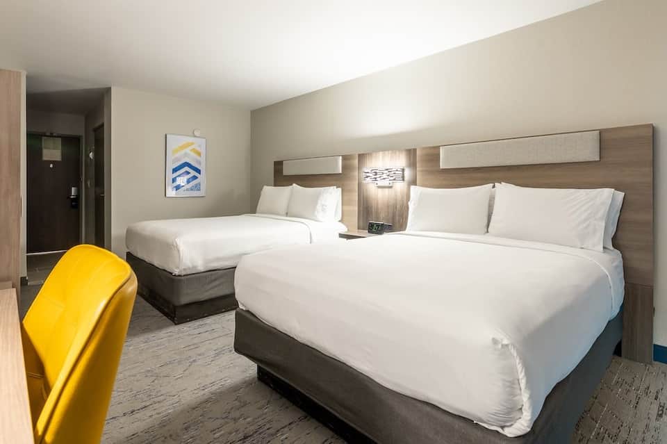 Hotel room with two queen beds, yellow accent chair, wooden headboards, and contemporary furnishings