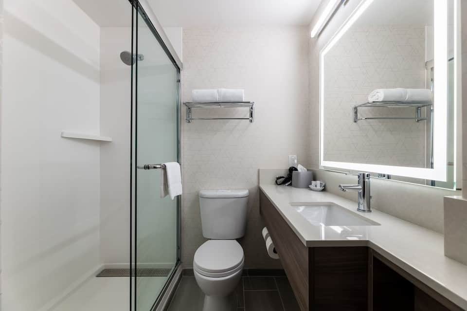 Clean bathroom with walk-in shower, white subway tile, illuminated mirror, and dark wood vanity