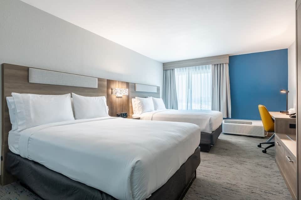Hotel room with two queen beds, blue accent wall, yellow desk chair, and natural light from windows