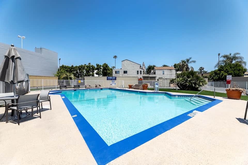 Outdoor swimming pool with bright blue deck, white safety fence, lounge chairs, and palm tree surroundings