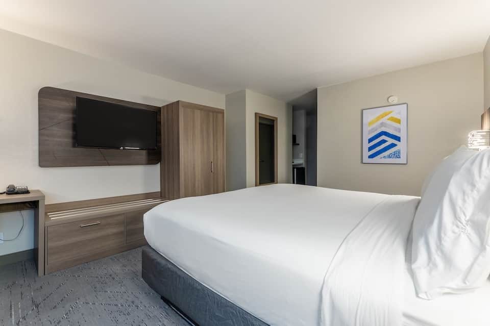 Contemporary hotel room featuring queen bed, wall-mounted TV, wood furnishings, and framed artwork