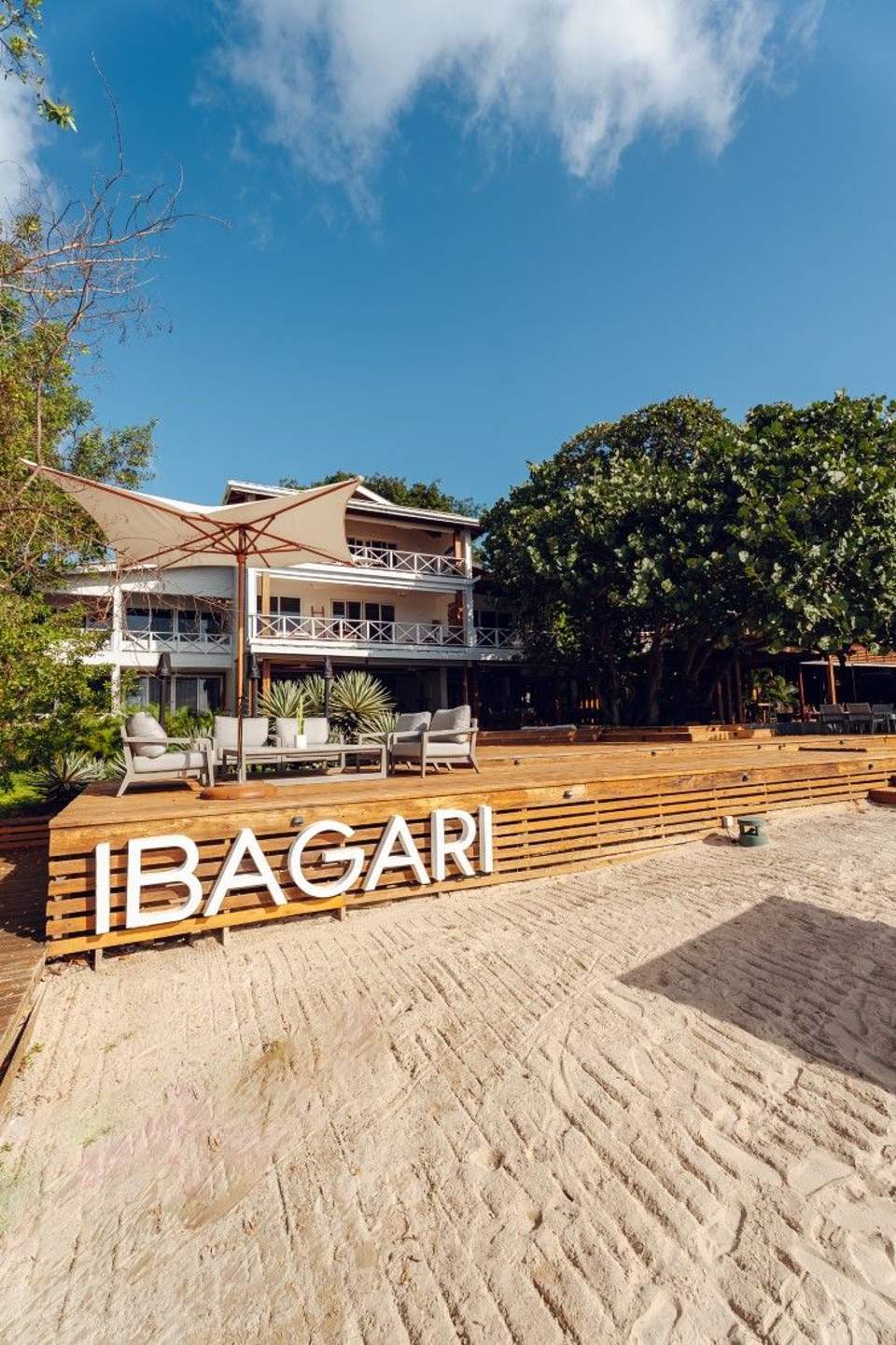 IBAGARI beachfront resort with two-story villa, wooden deck, umbrella seating, and sandy beach access