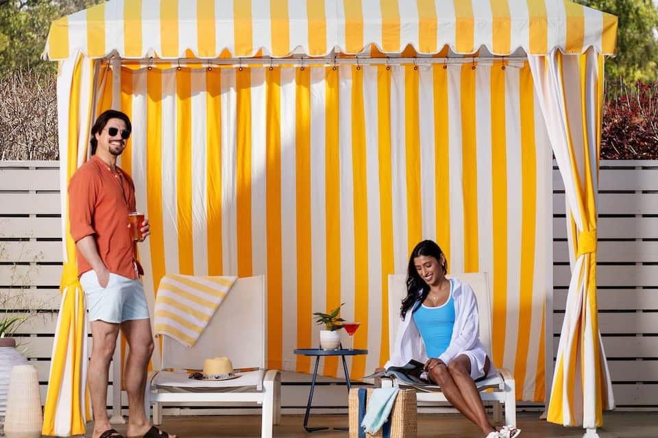 Couple relaxing in yellow and white striped cabana with lounge chairs and small table