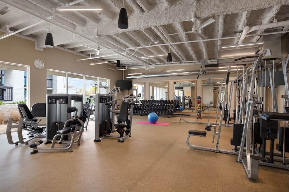 Spacious fitness center with cardio machines, weights, and windows overlooking grounds