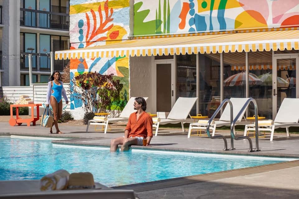 Woman at pool edge with colorful mural and yellow striped awning backdrop