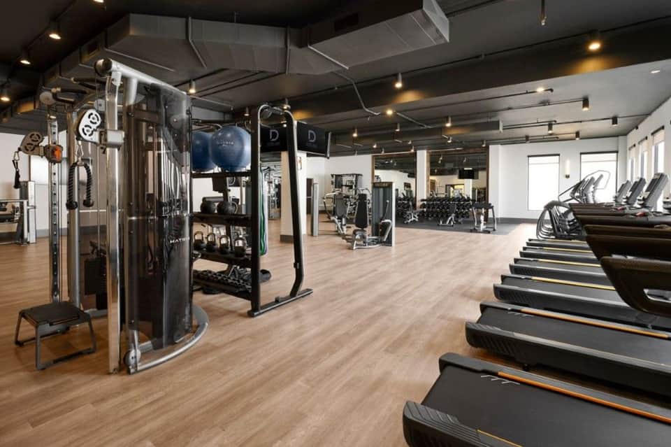 Modern fitness center with exercise equipment, cardio machines, and blonde wood flooring