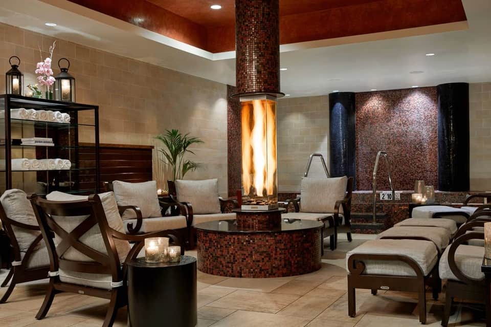 Luxurious spa relaxation area with central fireplace, lounge chairs, and mosaic tile accents