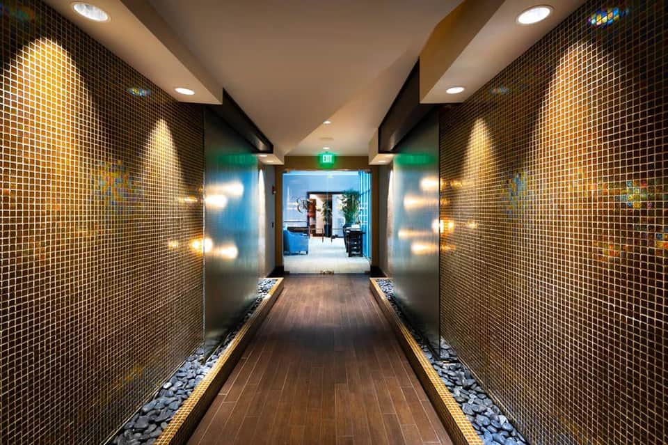 Modern hallway with golden mosaic tile walls, recessed lighting, and green exit sign