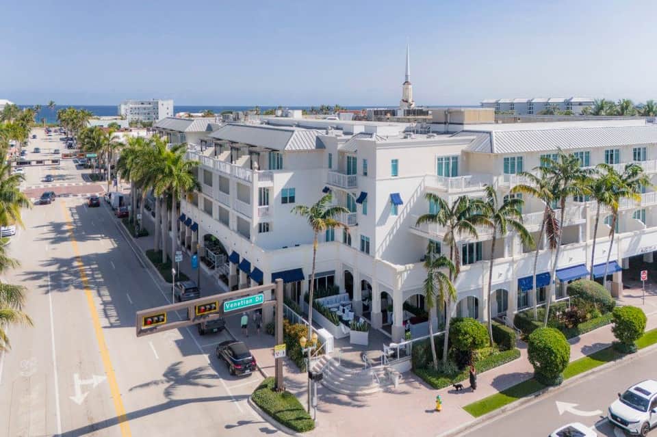 White beachfront resort buildings with blue accents and palm trees lining a street near the ocean
