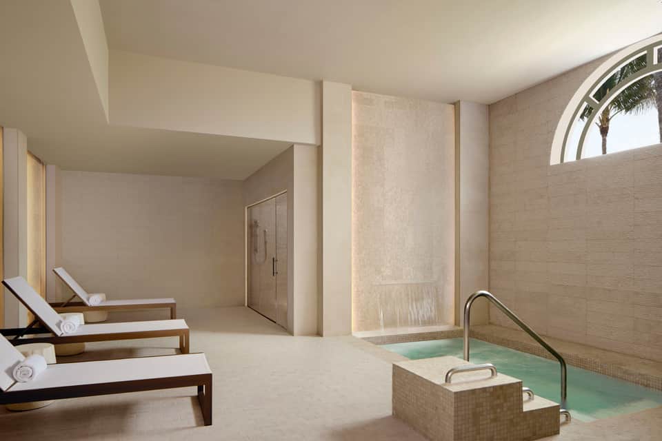 Luxury spa area with wooden loungers, rainfall shower, and light-filled bathing pool