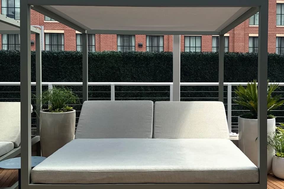 Modern gray pergola daybed with white cushions on rooftop terrace with city views