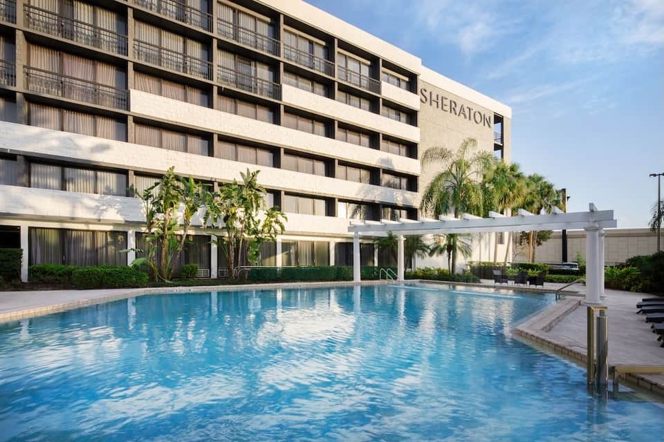 Sheraton hotel exterior with modern architecture, outdoor pool with shade structure, and manicured tropical grounds